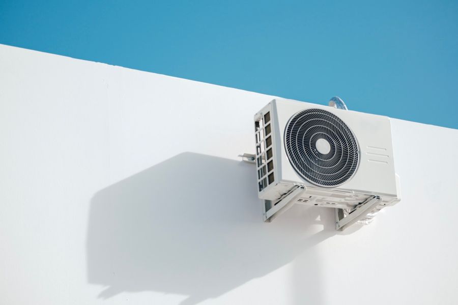 AC outdoor unit mounted on a white wall under a blue sky