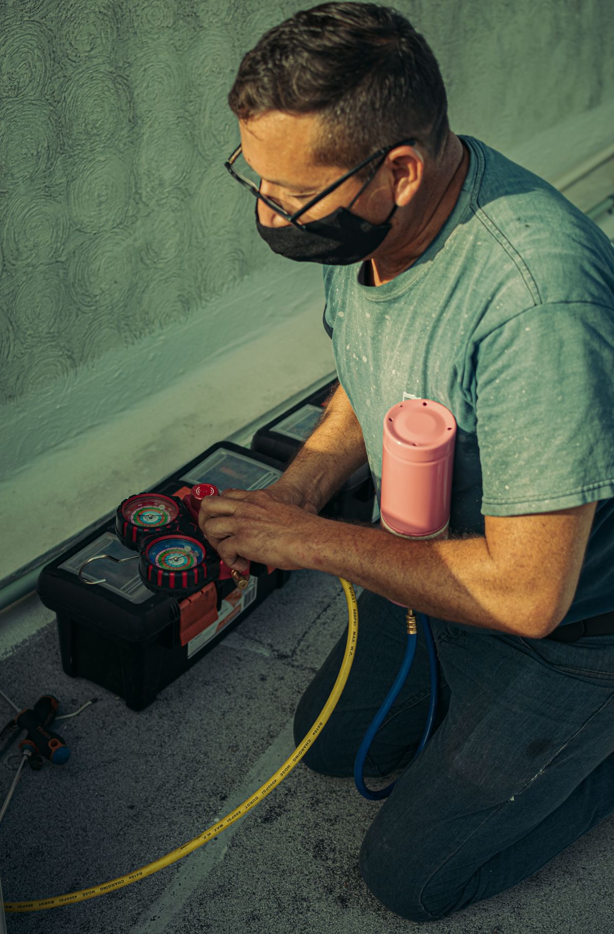 Technician kneeling to carry out AC maintenance with tools