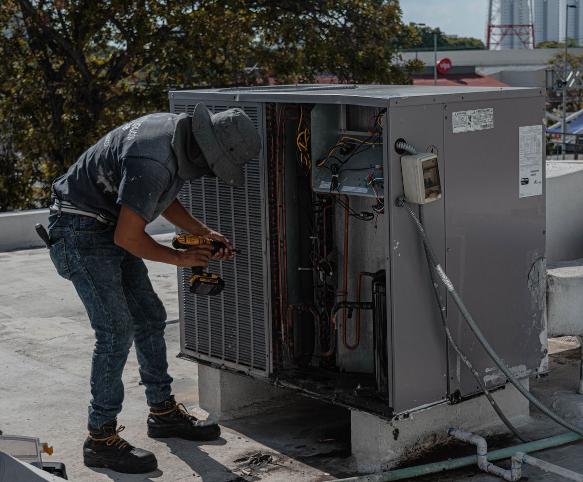 Technician in a bucket hat repairing a rooftop air conditioner