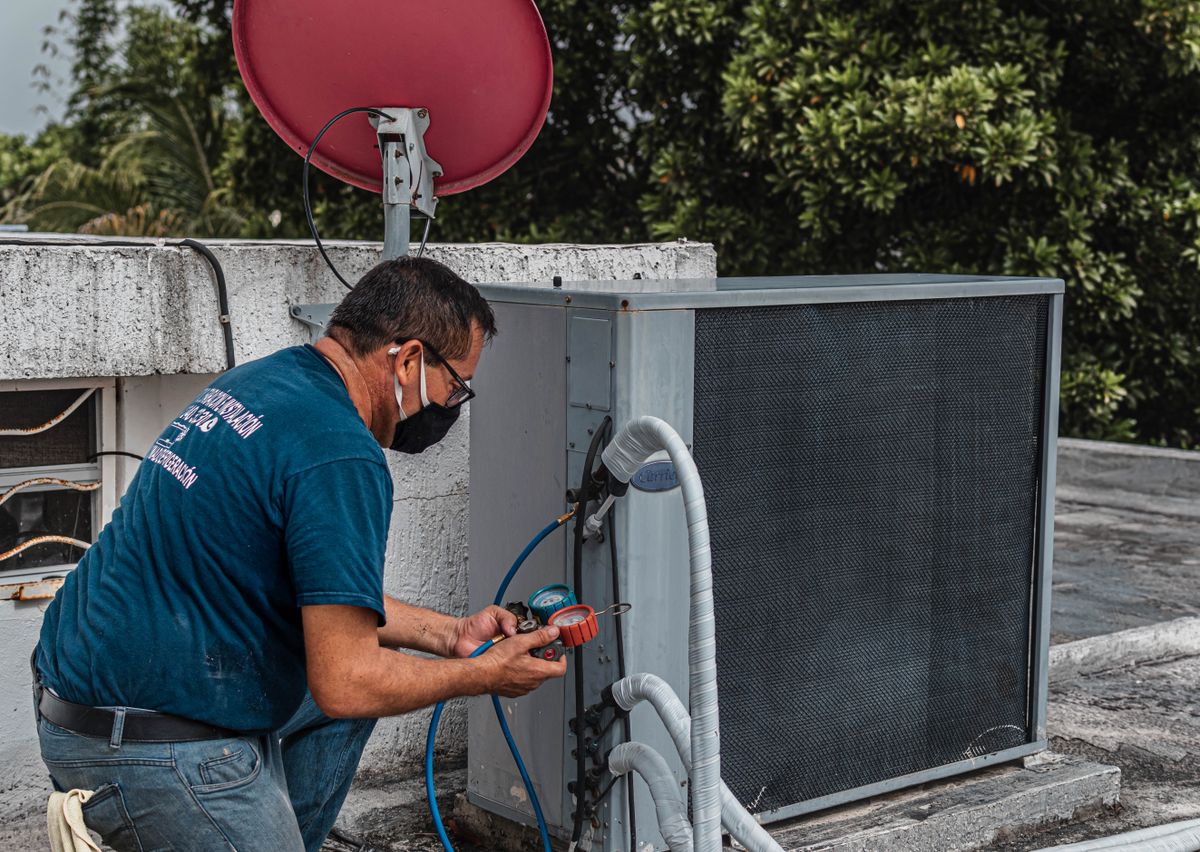 Technician using a manifold gauge on an outdoor AC unit